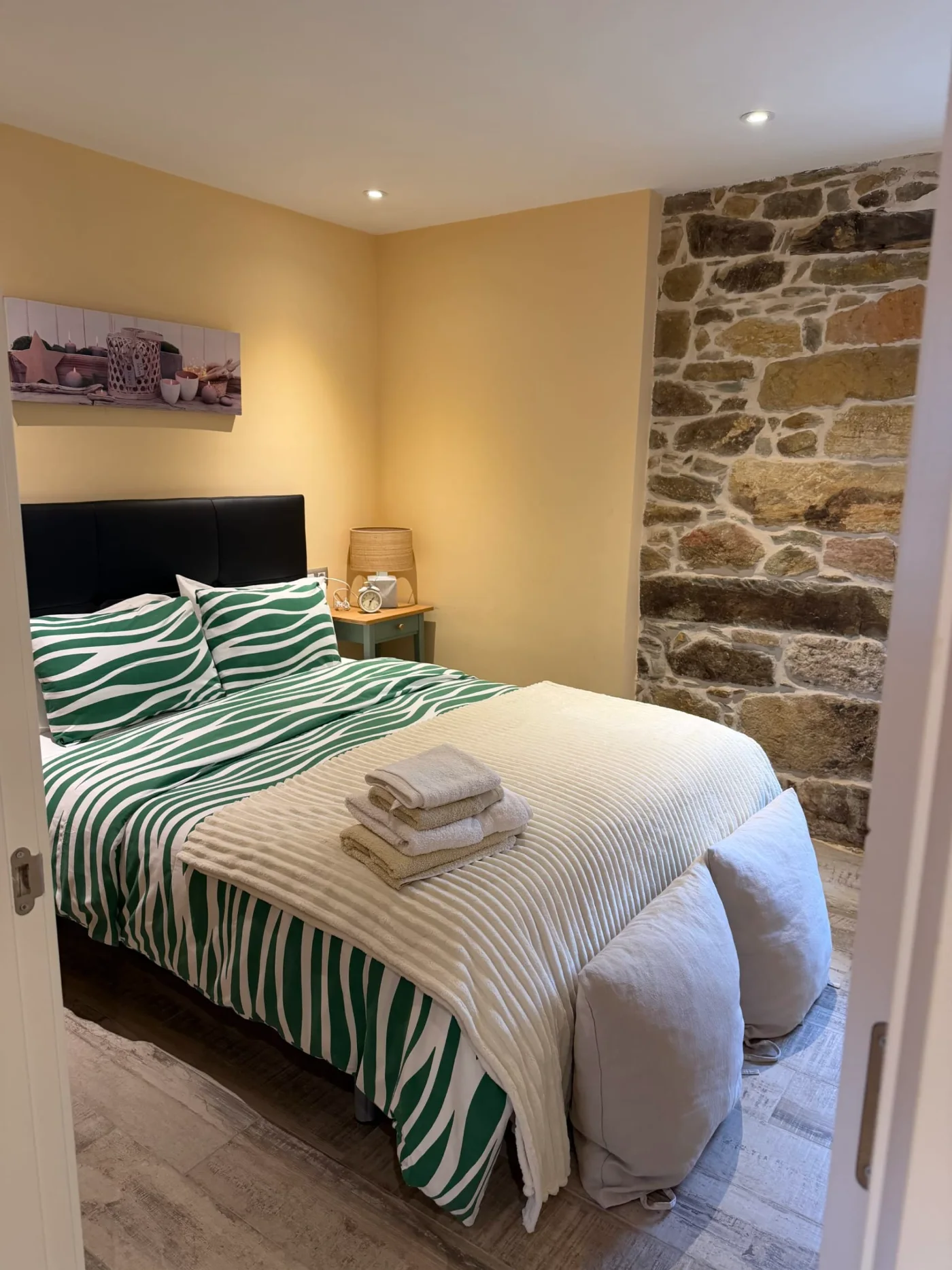Dormitorio con colcha verde y pared de piedra